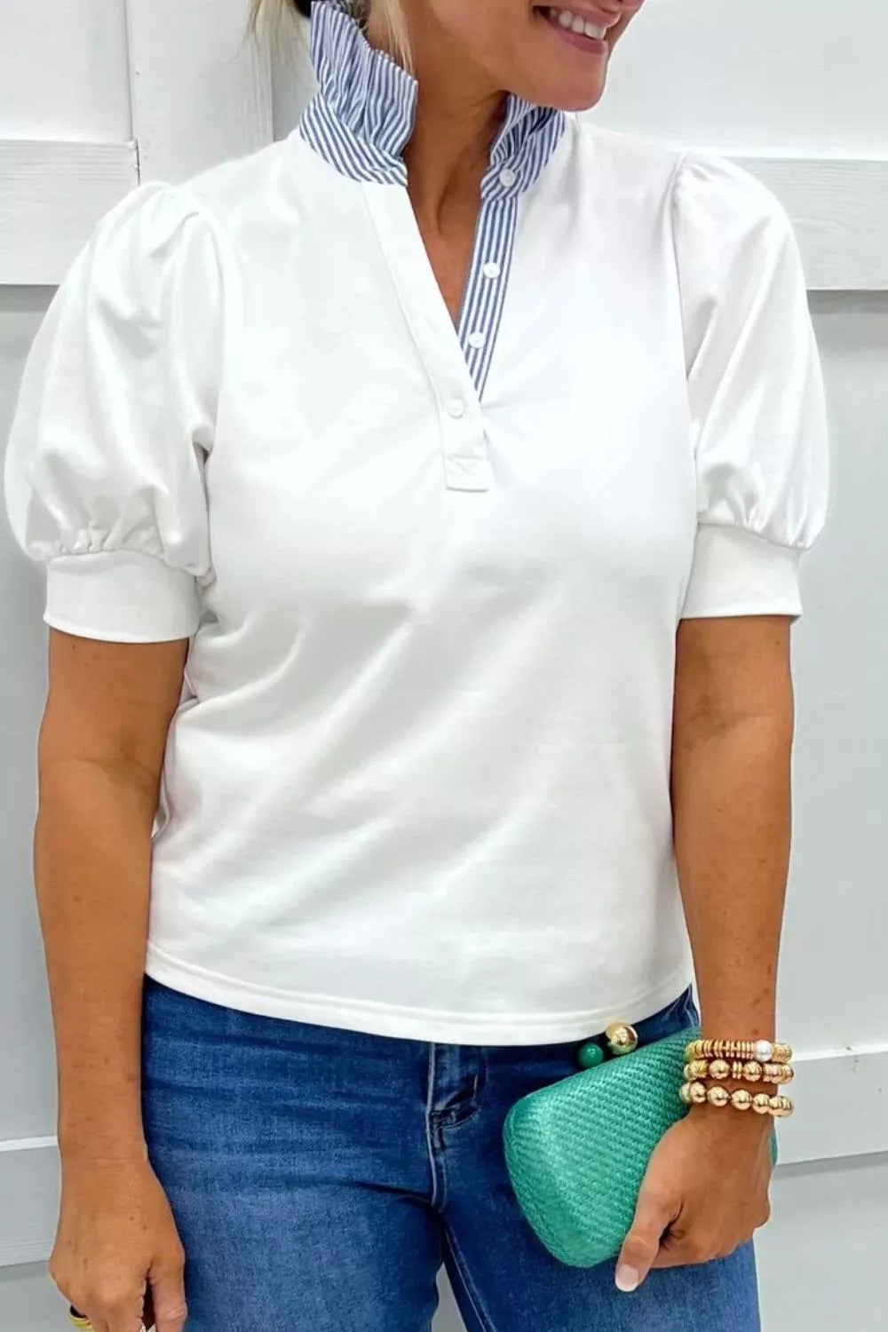 Person wearing a white blouse with puffed sleeves, blue jeans, and holding a green clutch.