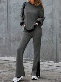 Person wearing a gray outfit with wide-leg pants against a concrete wall.