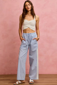 Woman wearing a white top and light blue checkered pants against a pink background