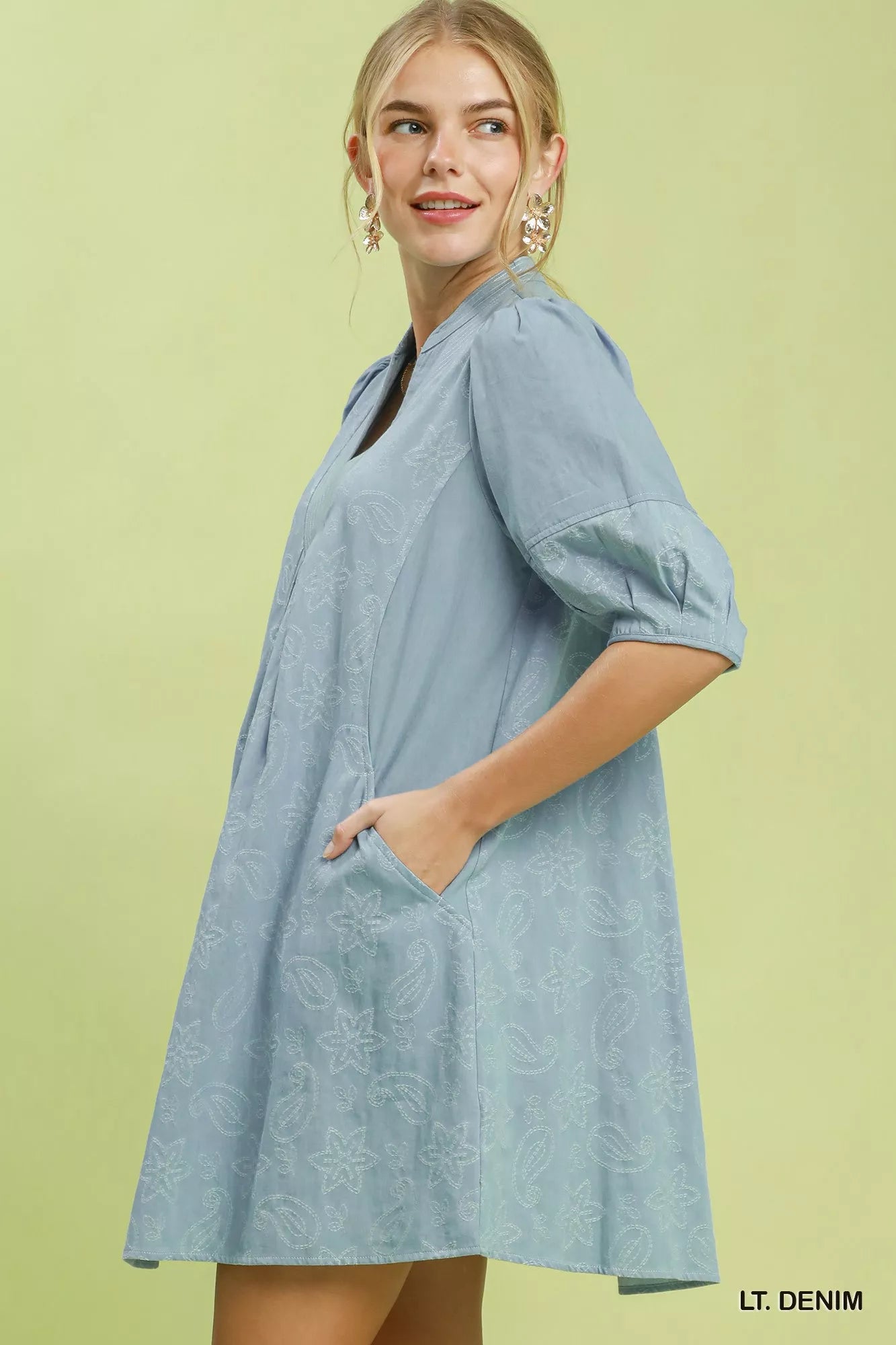 Woman wearing a light denim dress against a green background