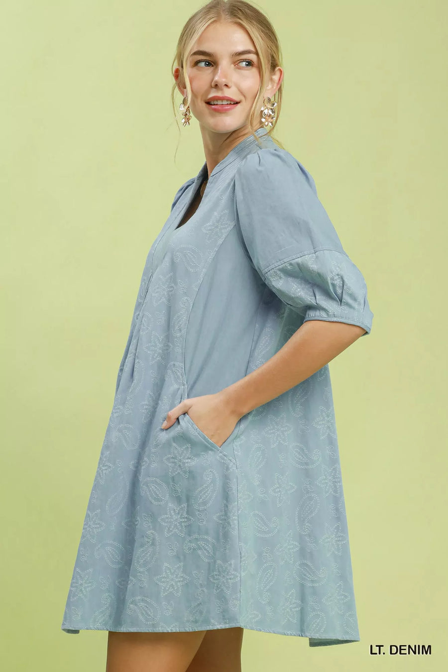 Woman wearing a light denim dress against a green background