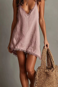 Woman wearing a pink slip dress holding a woven bag against a neutral background
