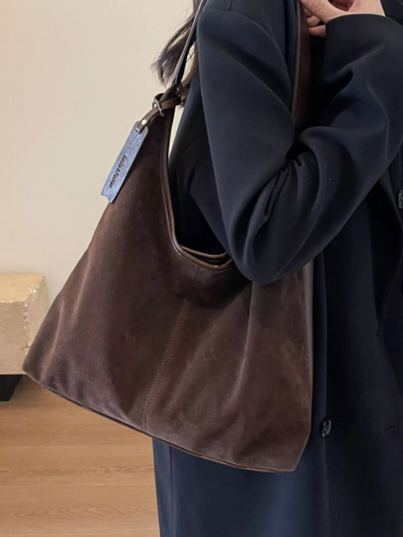 Person holding a brown leather handbag with a visible brand tag.