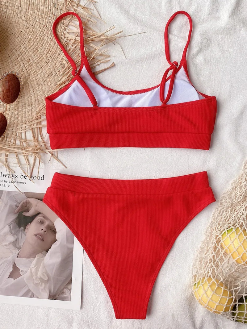 Red bikini set on a textured surface with a magazine and fruit in the background