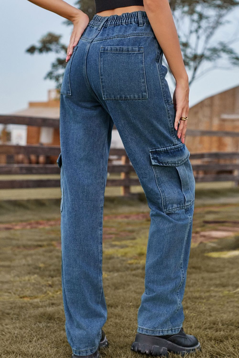 Person wearing blue jeans standing outdoors with a wooden fence and trees in the background