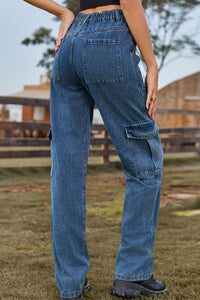 Person wearing blue jeans standing outdoors with a wooden fence and trees in the background