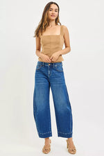 Woman wearing a beige top and blue jeans on a white background