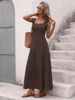Woman in a brown polka dot dress standing on stone steps with a textured wall and door in the background.