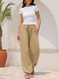 Woman wearing a white top and beige wide-leg pants standing in front of a white archway.