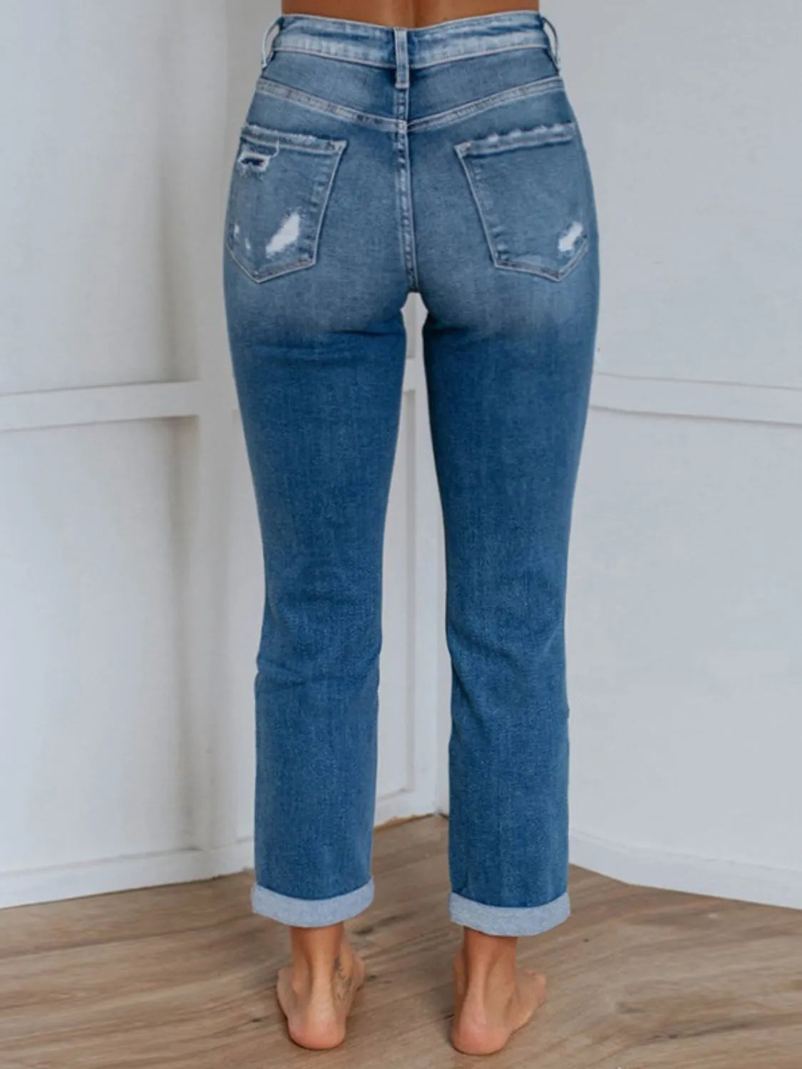 Blue jeans with a distressed look worn by a person on a plain background