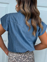 Person wearing a blue denim shirt with a white door background