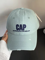 Light blue cap with 'CAP' and text held by a hand against a neutral background