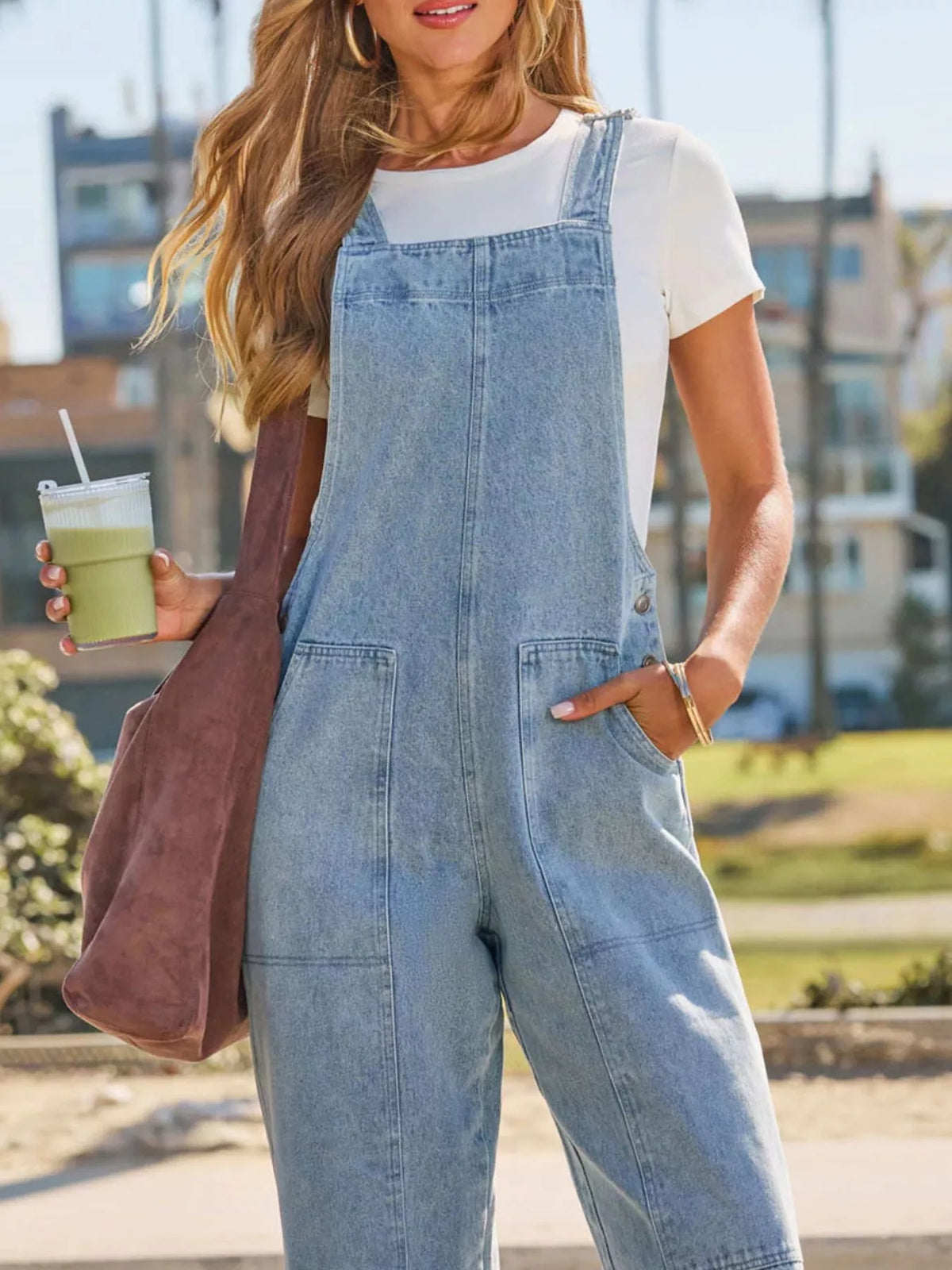 Person wearing denim overalls holding a drink outdoors