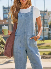Person wearing denim overalls holding a drink outdoors