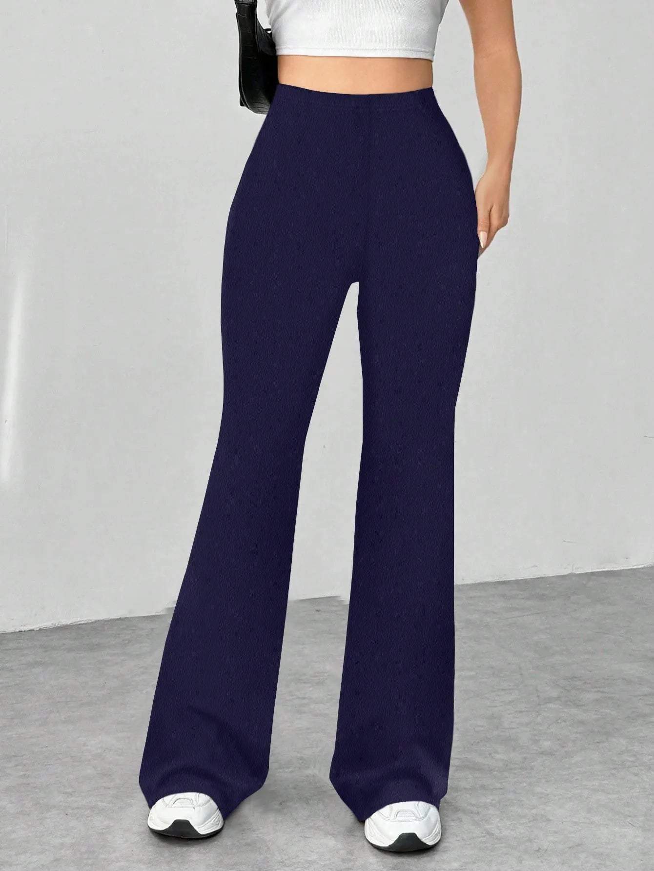 Navy blue flared pants worn by a person on a gray floor with a white wall background