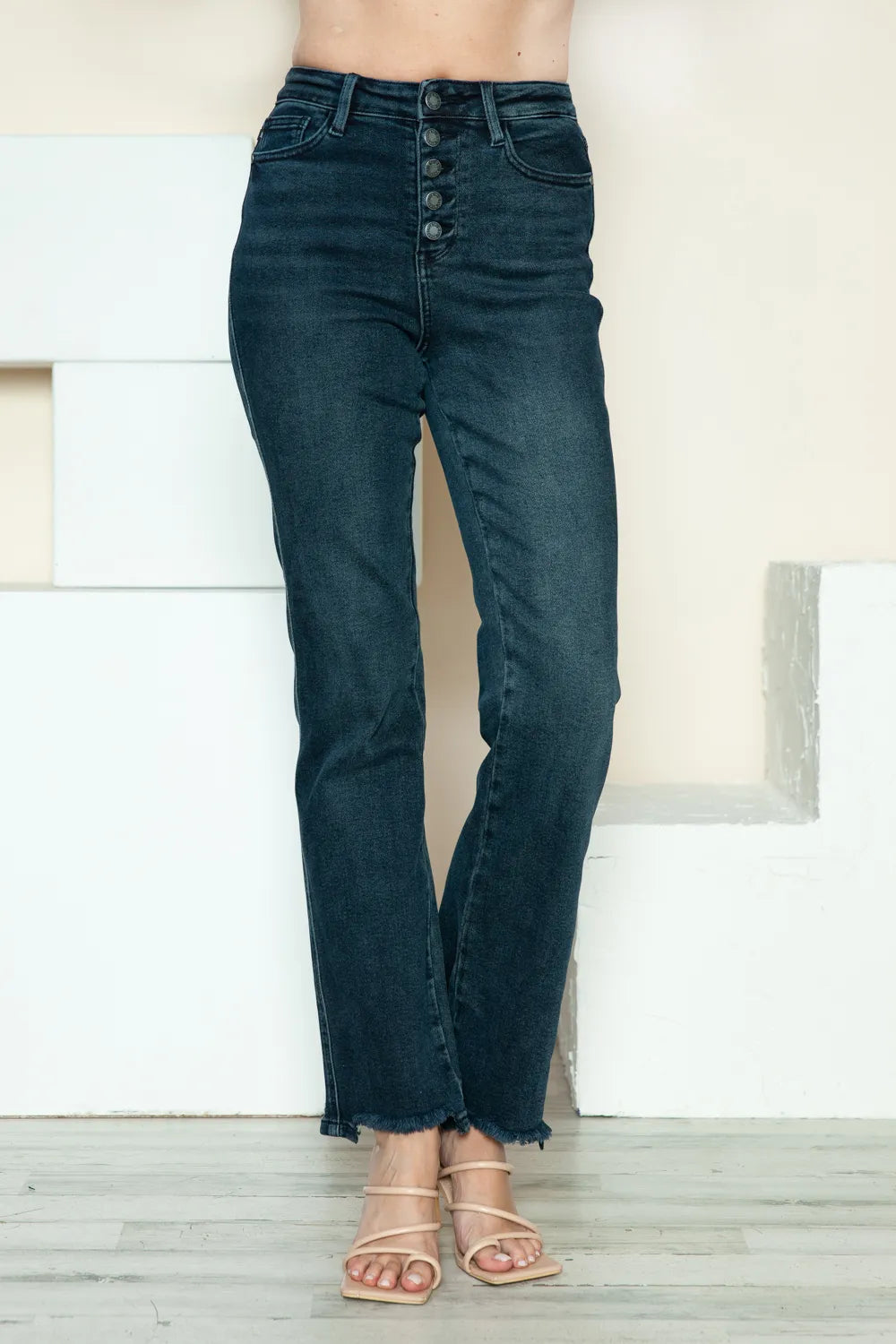 Dark blue jeans worn by a person on a light wooden floor.