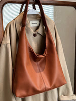 Brown leather handbag hanging on a beige jacket with a blurred background