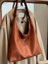 Brown leather handbag hanging on a beige jacket with a blurred background
