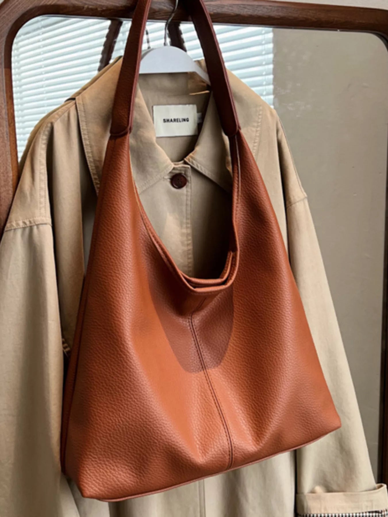 Brown leather handbag hanging on a beige jacket with a blurred background