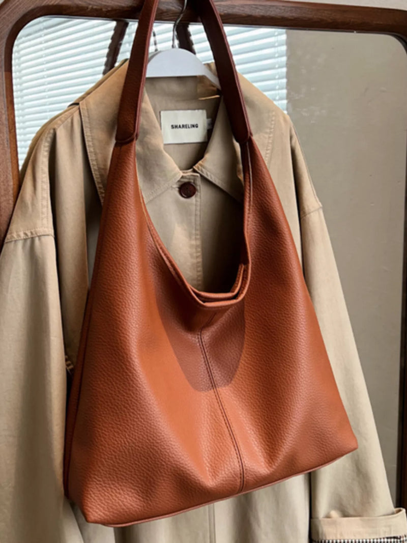 Brown leather handbag hanging on a beige jacket with a blurred background