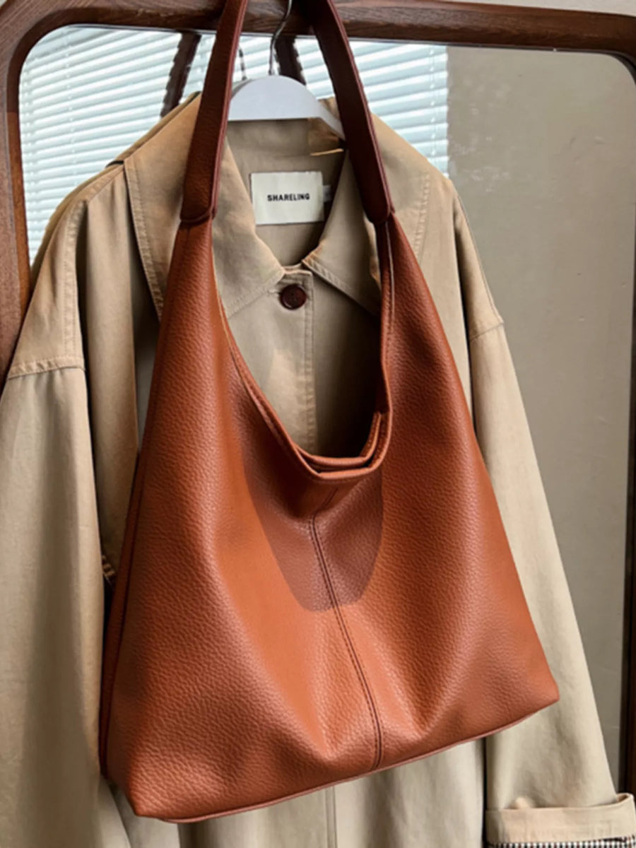 Brown leather handbag hanging on a beige jacket with a blurred background
