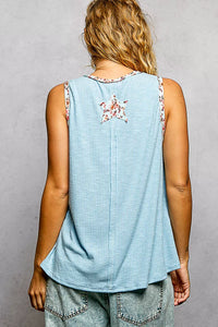 Person wearing a light blue sleeveless top with floral straps on a gray background