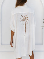 White cover-up with palm tree design worn by a person, against a white background