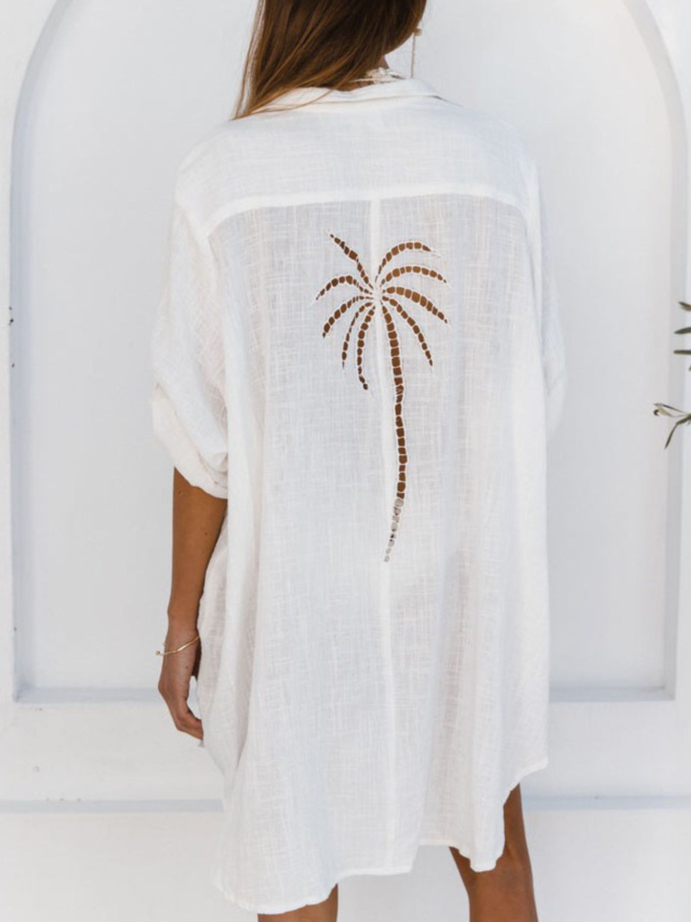White cover-up with palm tree design worn by a person, against a white background