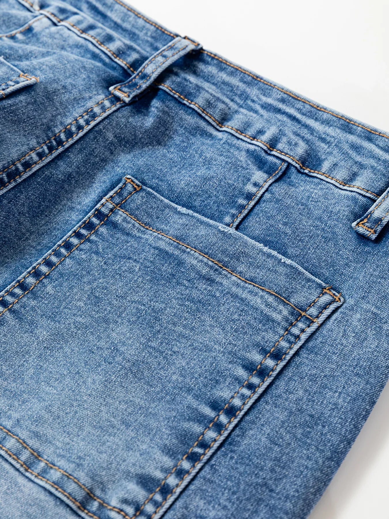 Close-up of blue denim jeans with stitching details on a white background