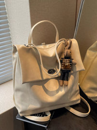 Beige handbag with a small plush toy attached, placed on a surface.