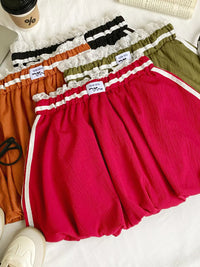 Set of colorful shorts on a white surface with a coffee cup and sneaker in the background.