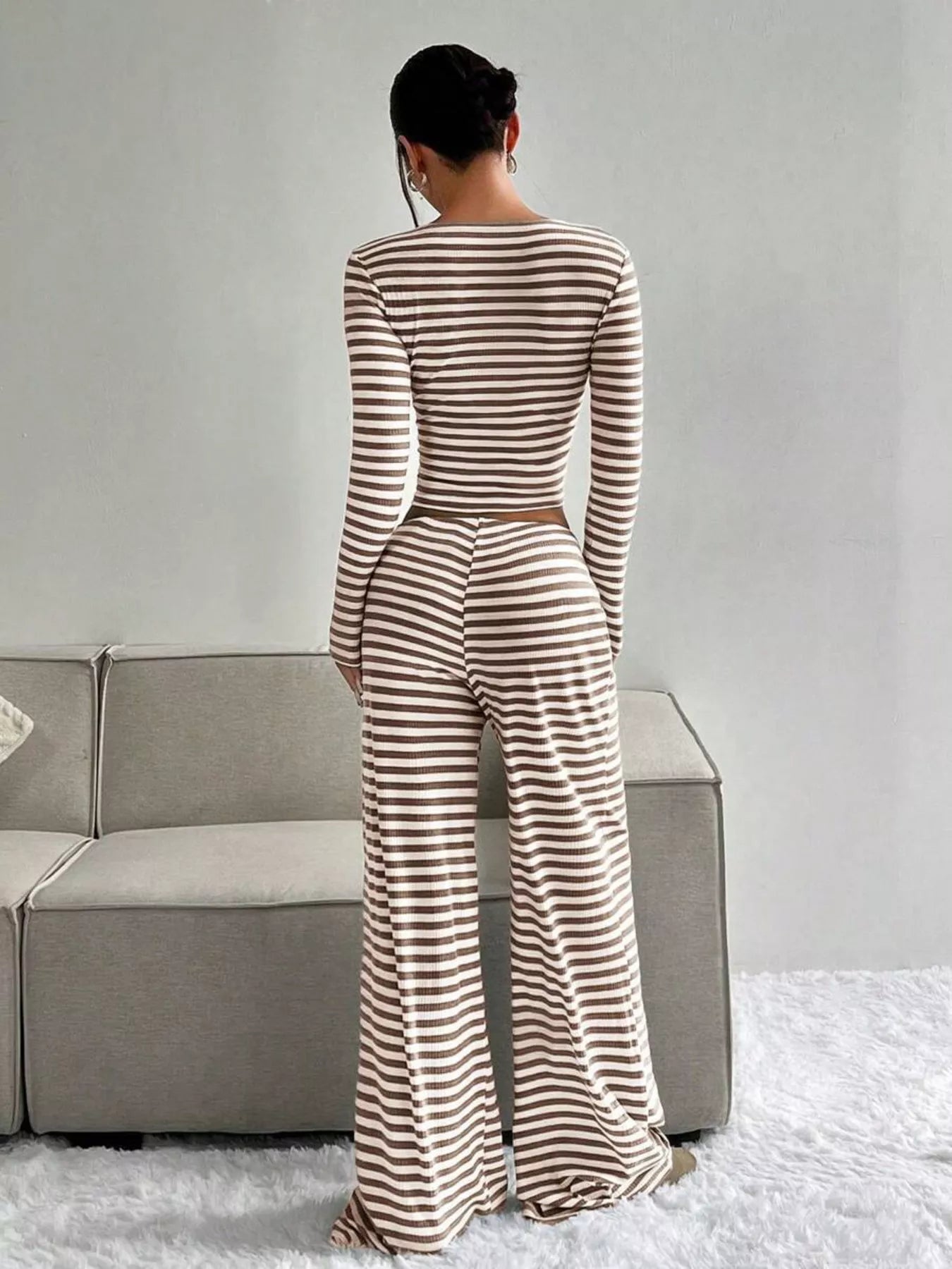 Person wearing a striped jumpsuit standing in a room with a gray couch and white floor.