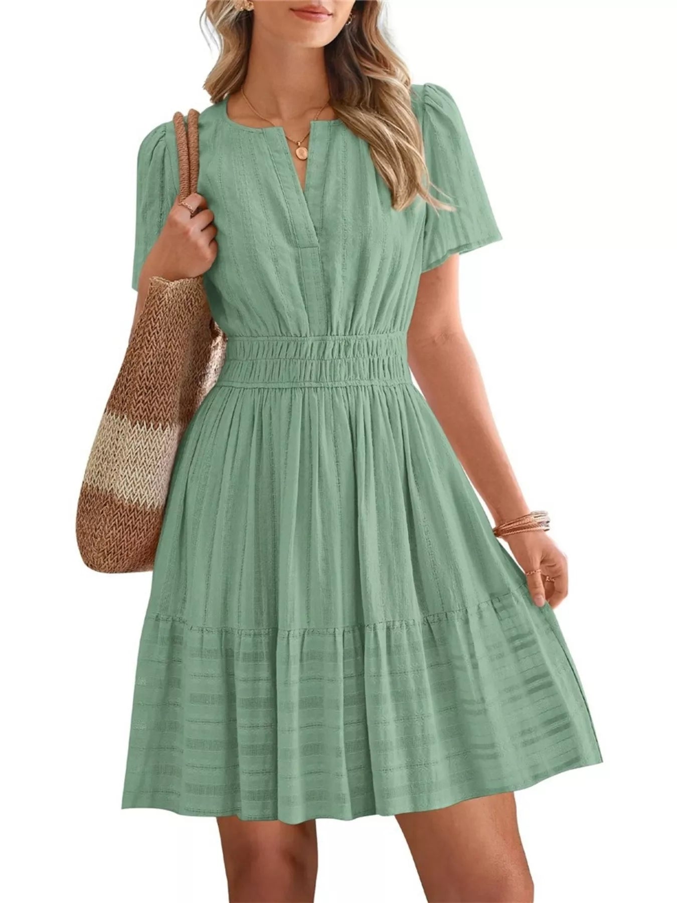 Woman wearing a green dress holding a woven bag on a white background