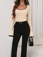 Woman wearing a beige long-sleeve top and black pants with a handbag on a light background