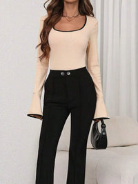 Woman wearing a beige long-sleeve top and black pants with a handbag on a light background