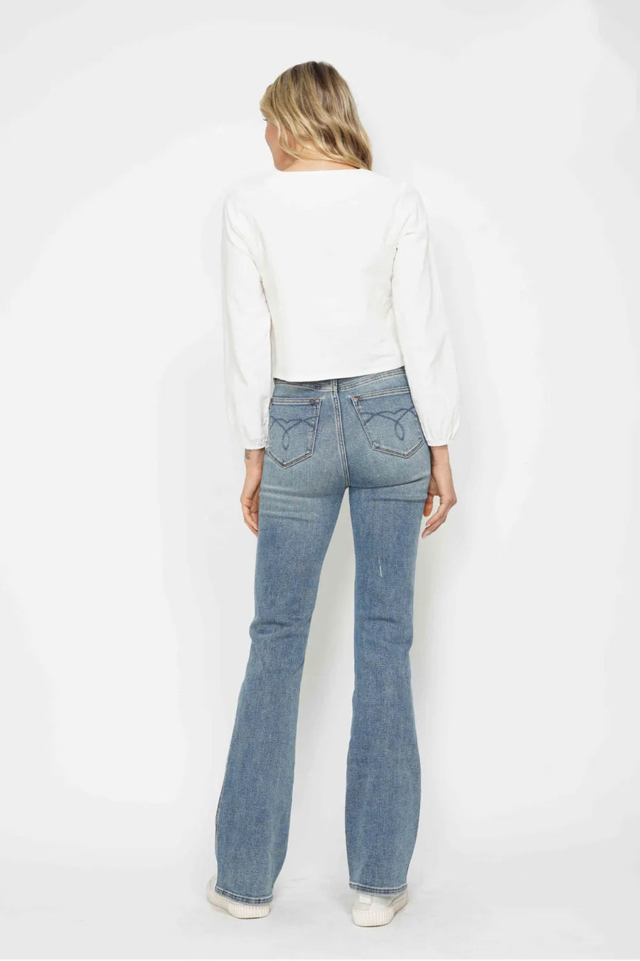 Person wearing light blue flared jeans and a white top on a white background
