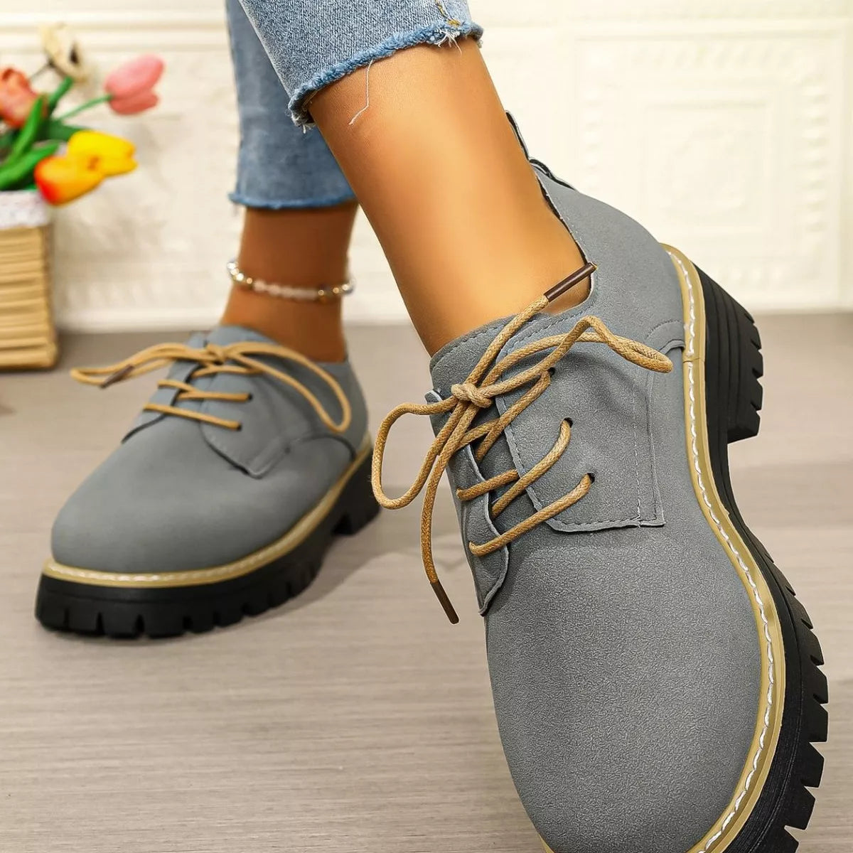 Gray shoes with brown laces worn by a person, with a blurred background.