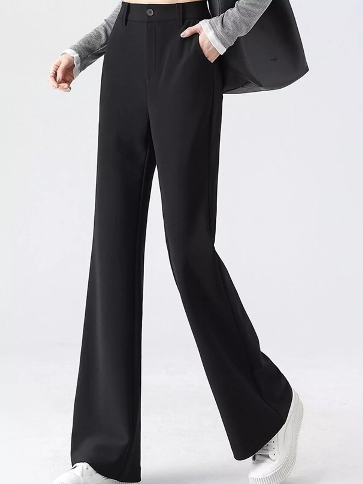 A model wearing black wide-leg trousers with a button closure, paired with a gray long-sleeve top, white sneakers, and a black shoulder bag against a light gray studio background.