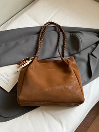 Brown leather handbag with braided handles on a gray surface