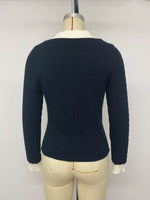 A dark navy blue cable-knit sweater with a white collar and white cuffs, displayed on a cream-colored dress form mannequin against a plain light gray background.