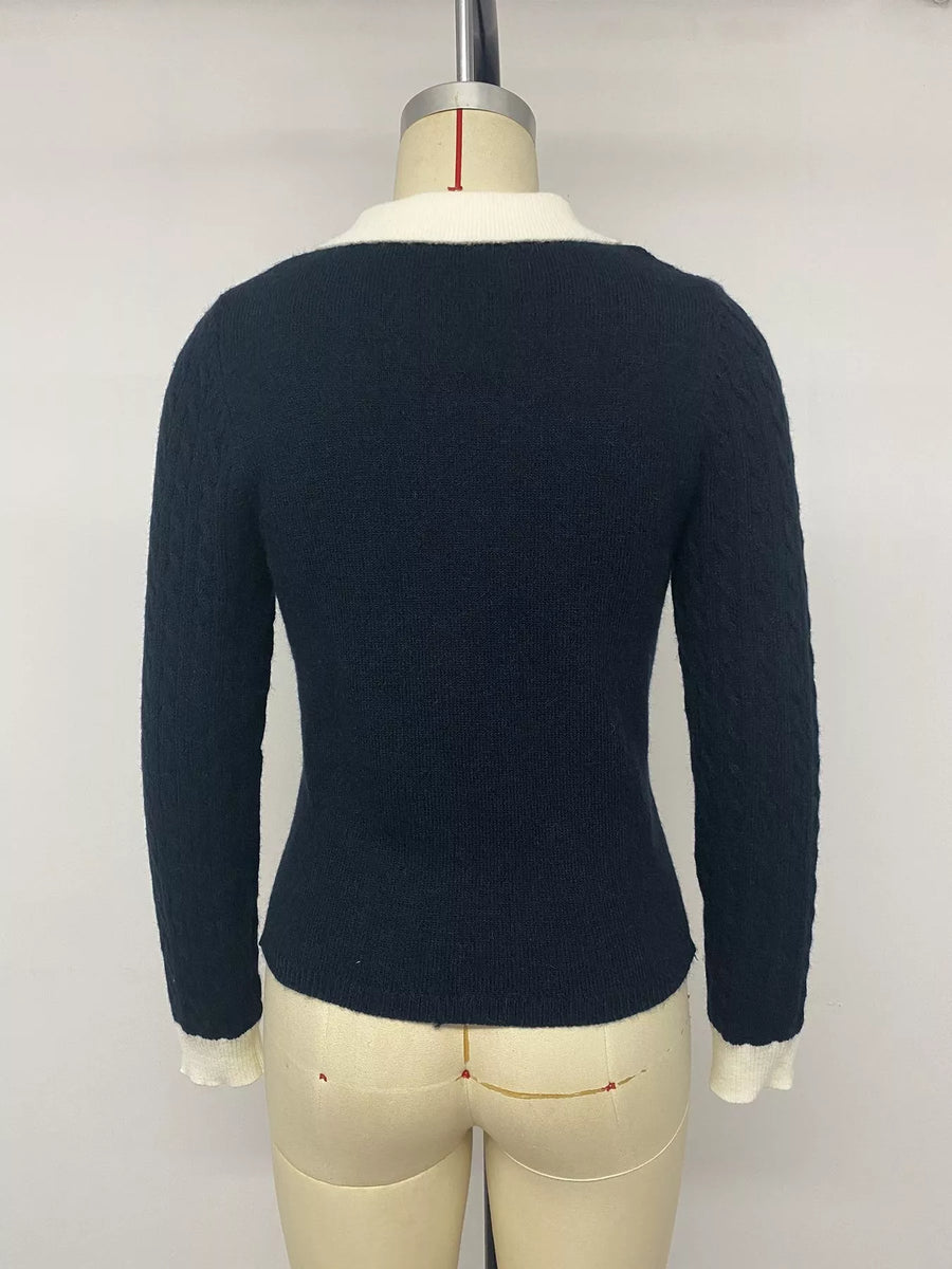 A dark navy blue cable-knit sweater with a white collar and white cuffs, displayed on a cream-colored dress form mannequin against a plain light gray background.