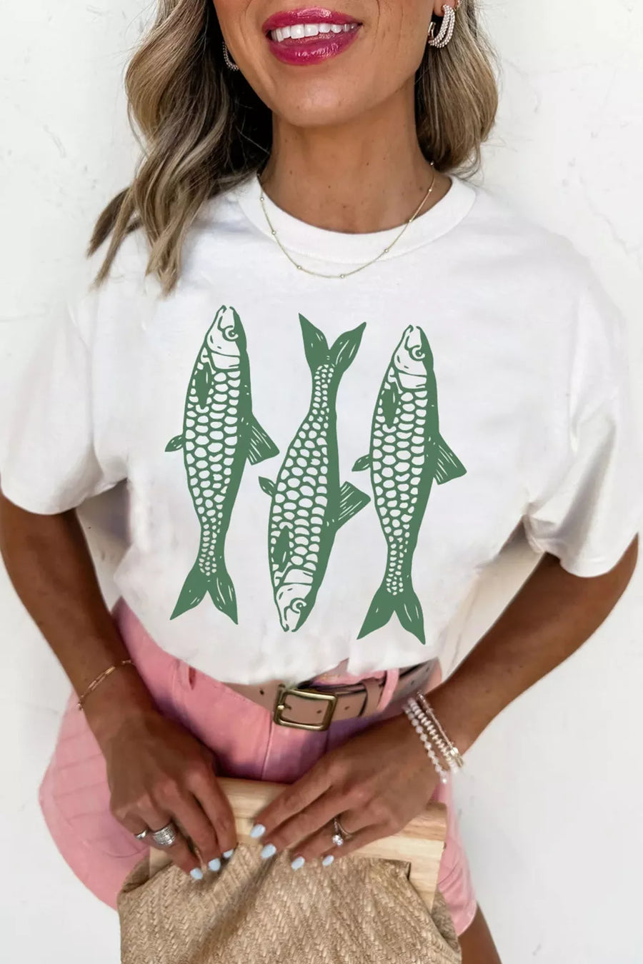 Woman wearing a white t-shirt with green fish graphics on a plain background