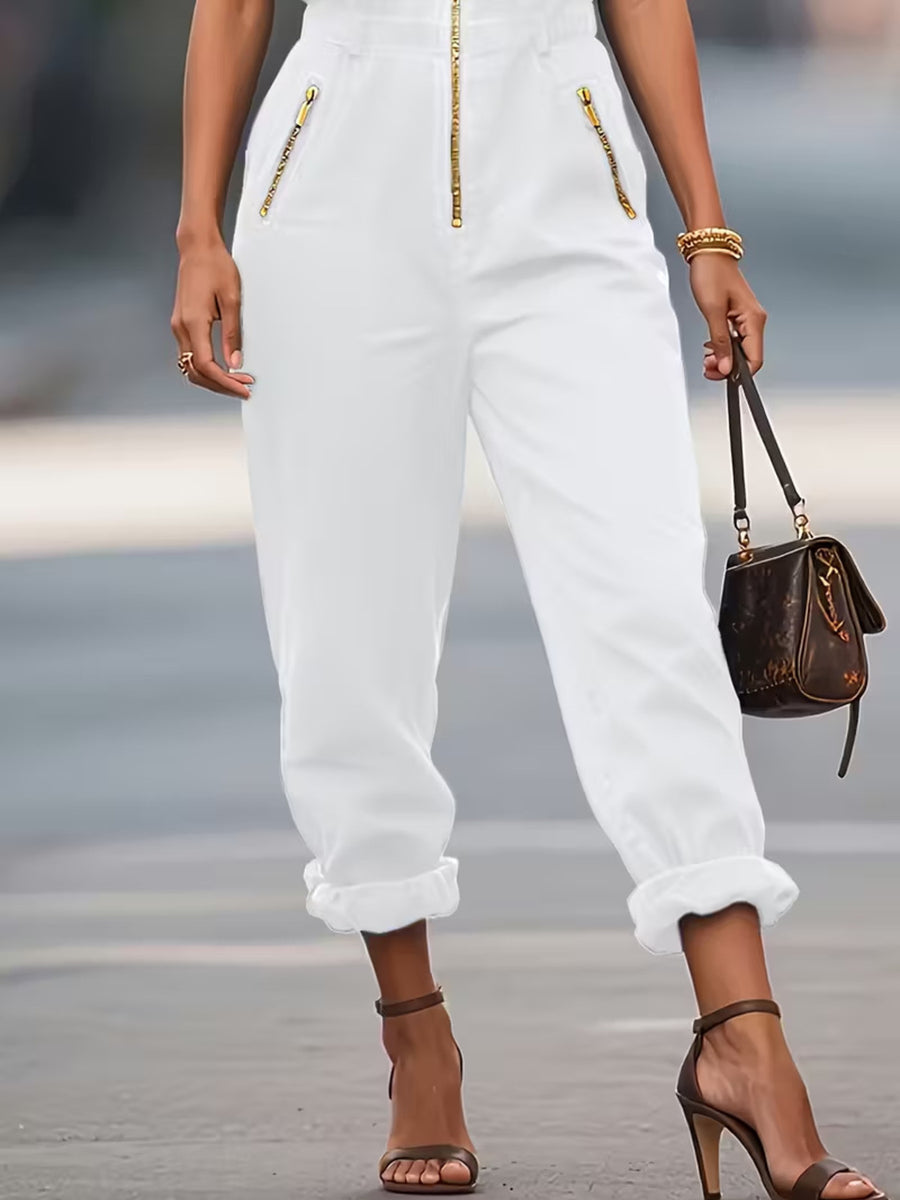 Person wearing white pants with gold zippers, holding a brown handbag on a blurred street background