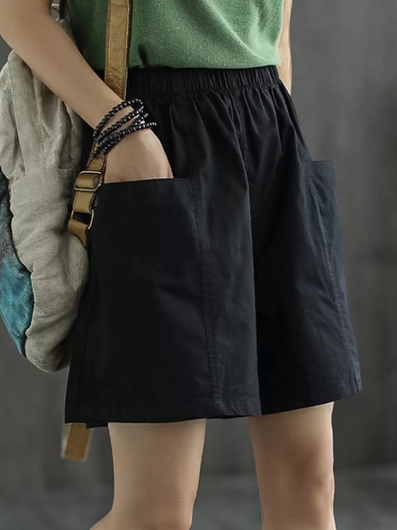 Person wearing a green top and black skirt holding a backpack against a gray background