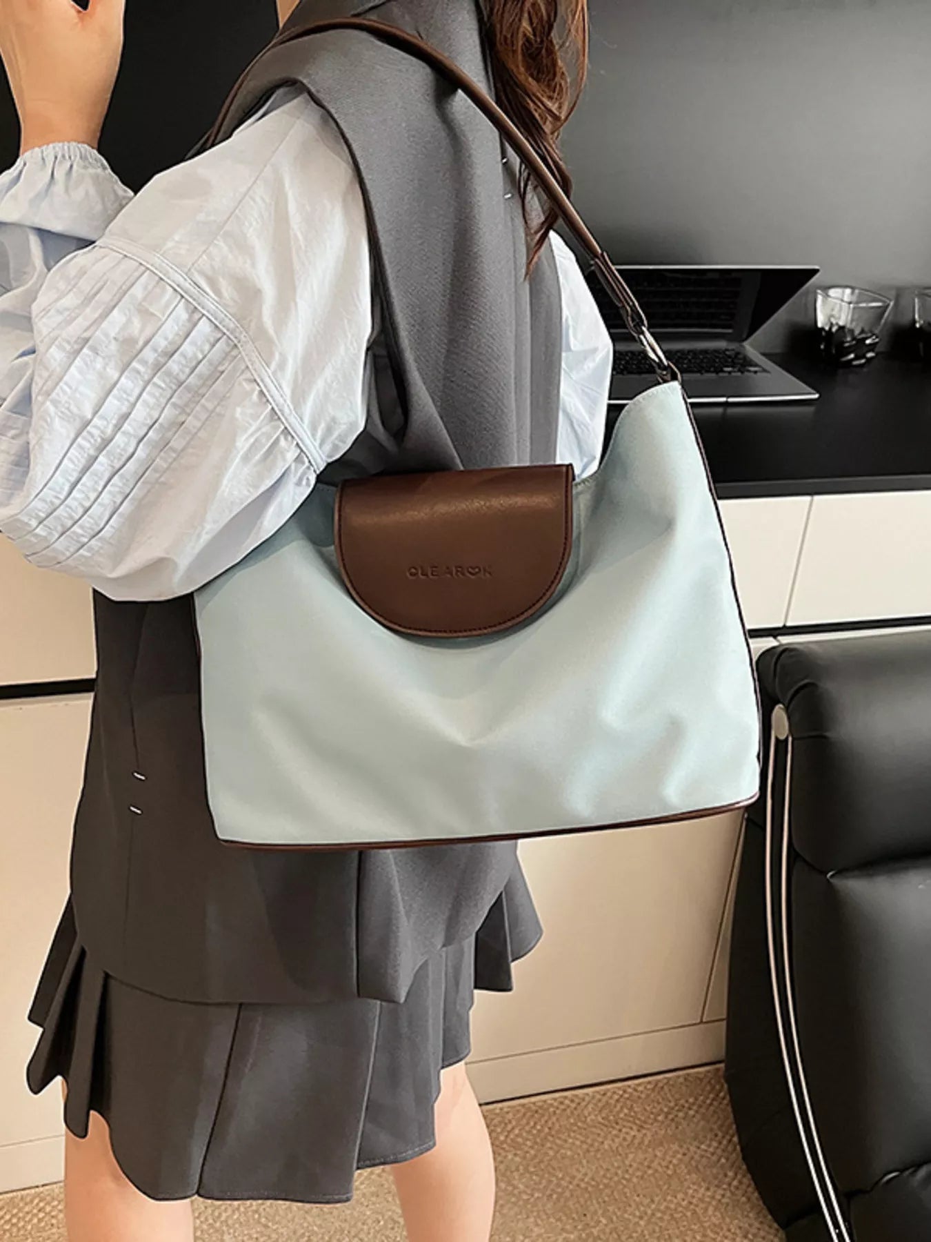 Person wearing a light blue handbag with a brown strap in an indoor setting
