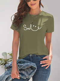 Person wearing a green t-shirt with 'Smile' text, holding jeans against a neutral background