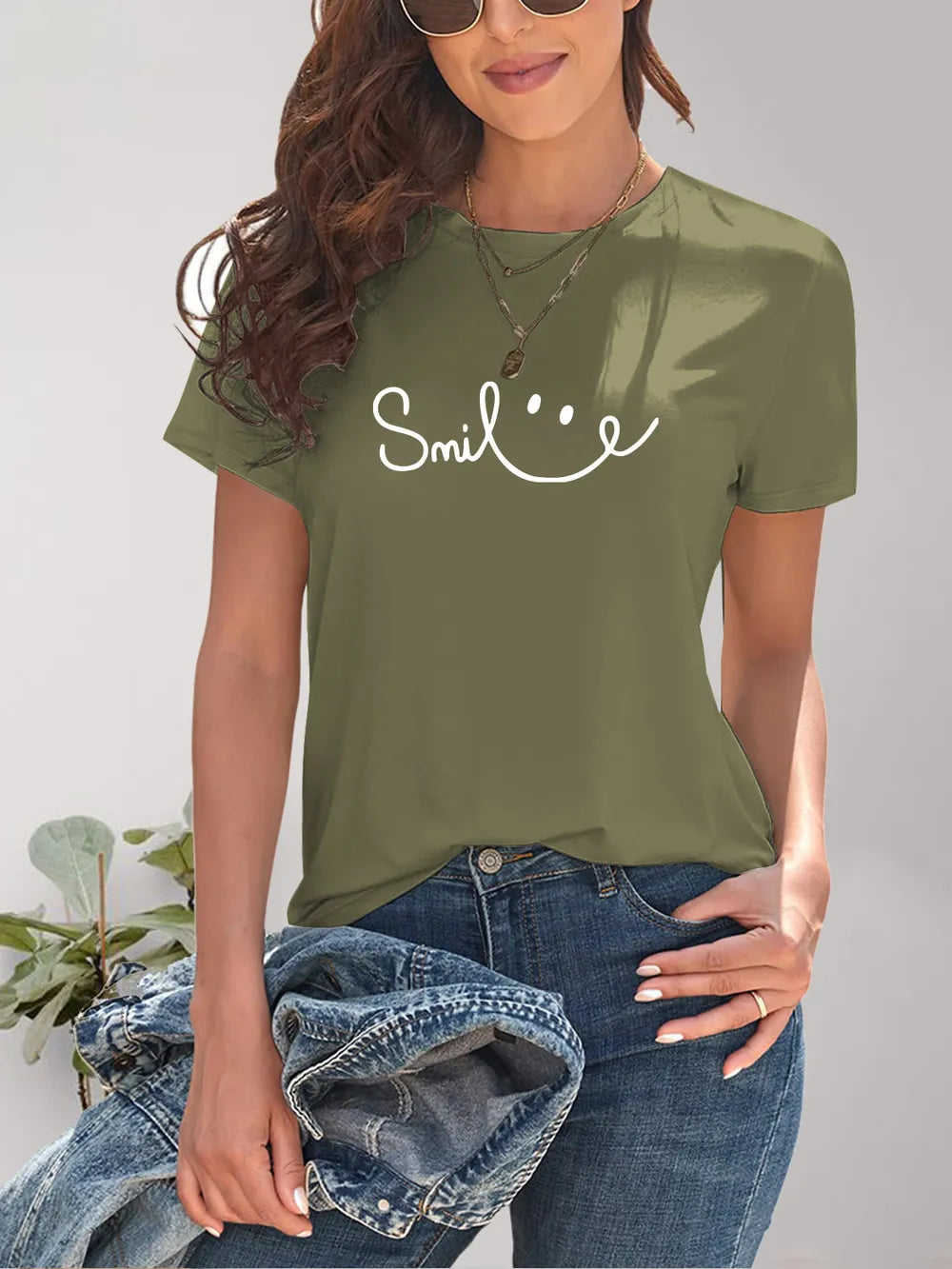 Person wearing a green t-shirt with 'Smile' text, holding jeans against a neutral background