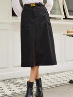 Person wearing a black skirt with a white shirt and black boots on a patterned rug.