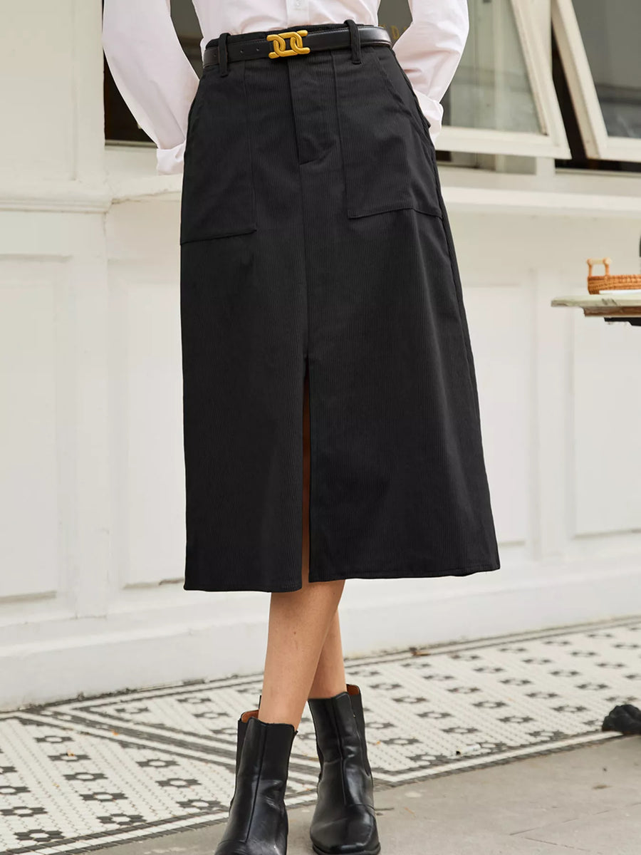 Person wearing a black skirt with a white shirt and black boots on a patterned rug.