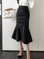 Person wearing a black ruched skirt with a white top and holding a white handbag.